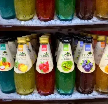 Colorful Mr. Basil basil seed drink bottles arranged on store shelves with turquoise background