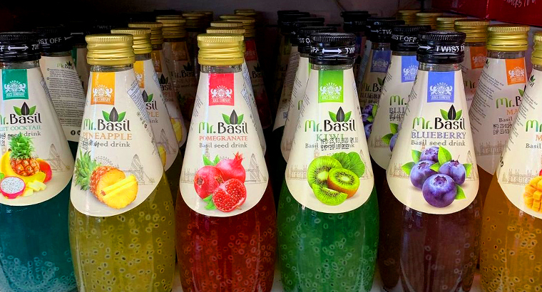 Close-up of 'Mr. Basil' fruit drinks on a shelf, highlighting the diverse fruit flavors like pineapple, pomegranate, and blueberry with visible basil seeds.