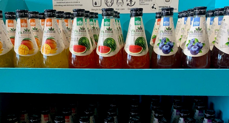 Multiple flavors of 'Mr. Basil' seed drinks organized on a blue retail shelf, showcasing mango, watermelon, and blueberry varieties.